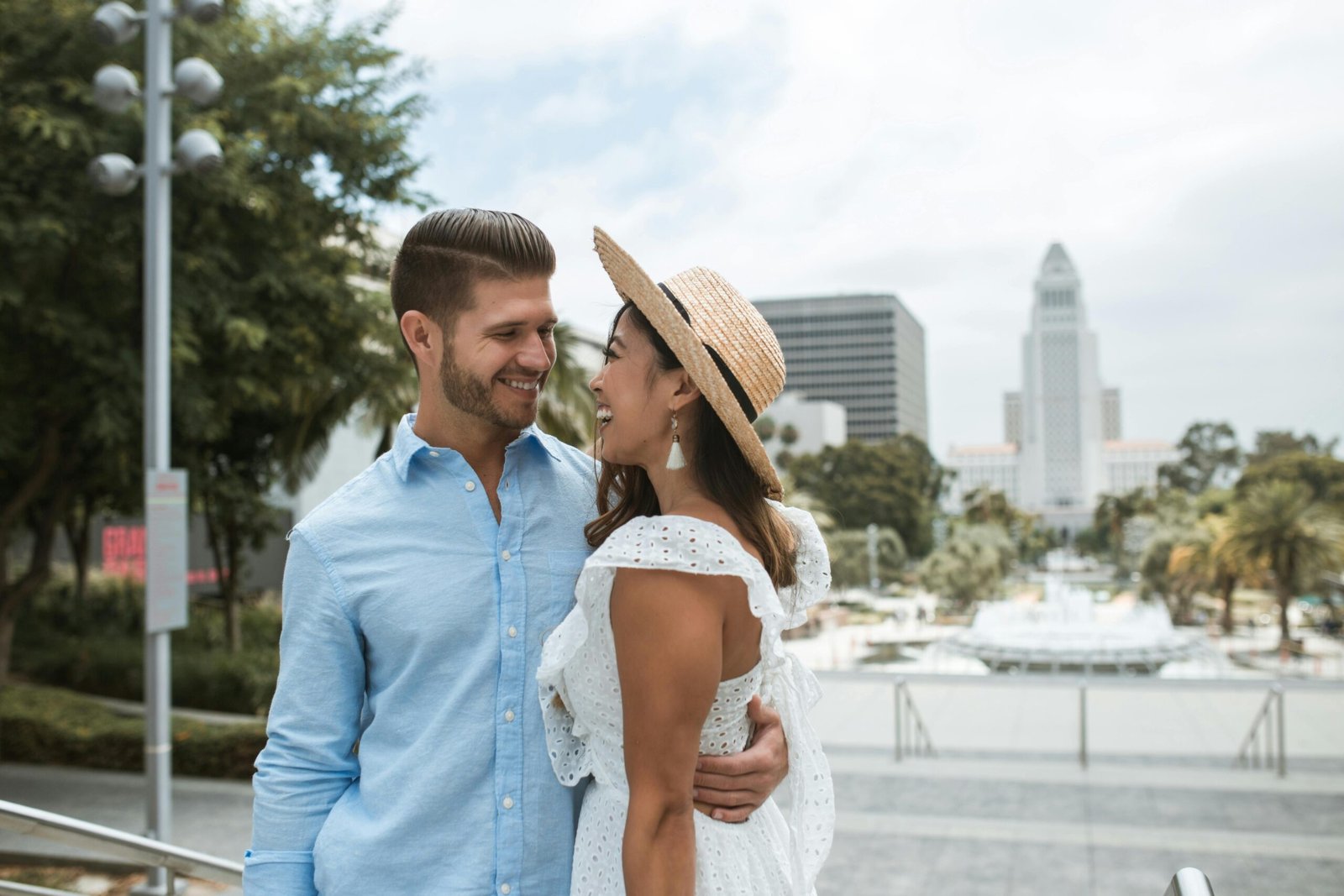Romantic couple embracing near iconic City Hall against a bright outdoor setting.